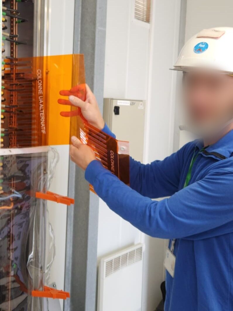 Un technicien range des câbles dans une armoire électrique avec un peigne orange imprimé en 3D